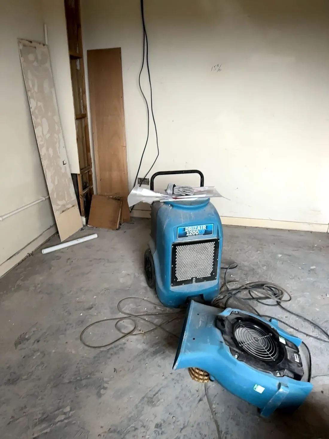A DriZair dehumidifier and air mover drying out a stripped, water-damaged room during insurance restoration